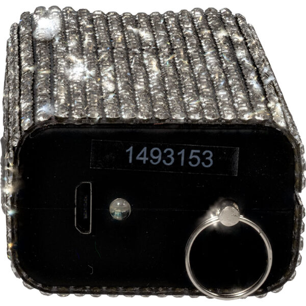 The image features a close-up view of a rectangular device embellished with rows of sparkling crystals. The top and sides are covered in a grid-like pattern of reflective gemstones, giving it a luxurious appearance. On the front of the device, there is a small dark panel with a number 1493153 printed on it. An indented slot is visible