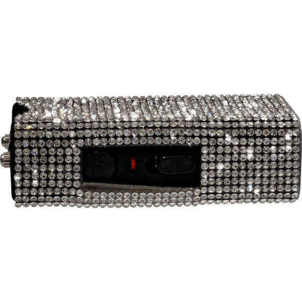 This image features a rectangular handheld device, likely a taser or stun gun, with a luxurious design. The entire surface is embellished with rows of sparkling clear rhinestones, giving it a glamorous and eye-catching appearance. The rhinestones are uniformly aligned, covering the device completely except for a central panel that contains buttons and an indicator light. The contrast between