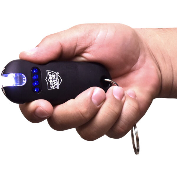 The image depicts a hand holding a compact personal defense tool designed as a small stun gun. The device has a rubberized, black exterior with a sleek, ergonomic design, fitting comfortably in the hand. It features a prominent brand logo, Streetwise, visible on its surface. The front end of the device emits an electric arc with a blue light