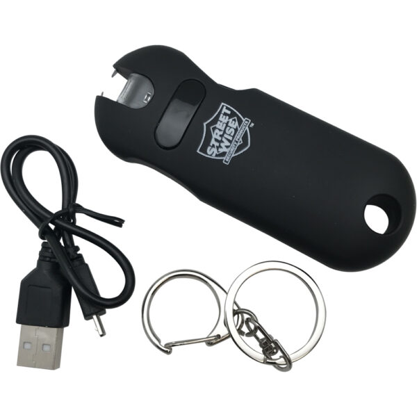 This image features a black personal safety stun gun, designed for self-defense. The device has a sleek, compact design and features branding on its surface. Situated next to the stun gun is a USB charging cable, displaying its compatibility with electronic charging methods. The image also includes two metal key rings, suggesting portability and ease of attachment to keychains or bags