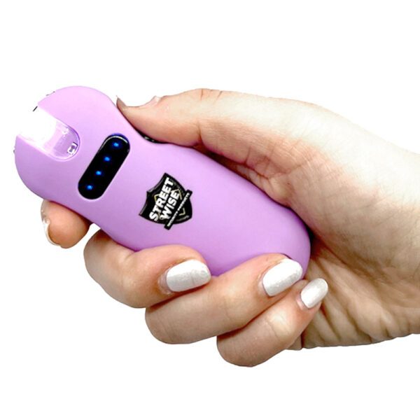 The image shows a person holding a small, handheld stun gun with a light purple casing. The device features the brand name Street Wise on a logo positioned prominently on its body. There are several small blue LED lights on the device, possibly indicating battery status. The person holding the stun gun has neatly manicured nails painted white. The stun gun