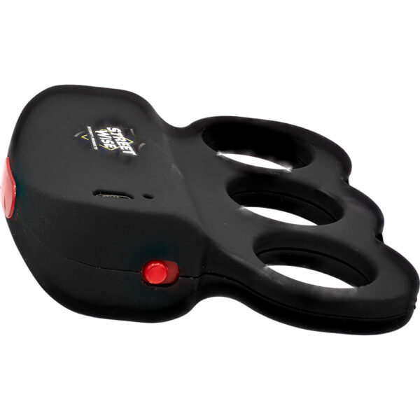 The image shows a compact, black self-defense tool designed in the shape of knuckles with two finger holes. The device features a red button on the side and a small charging port, suggesting it's an electronic gadget. The top of the device is branded with Street Wise indicating the manufacturer or product name. Its ergonomic design suggests it fits comfortably in