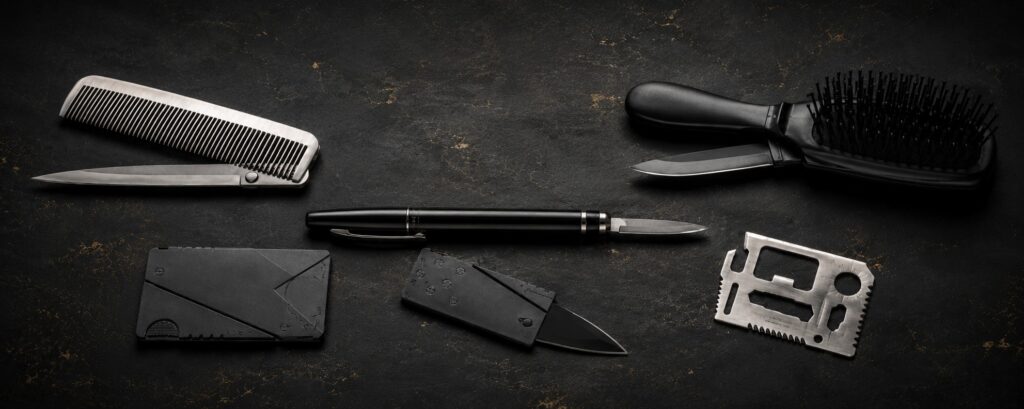 Disguised self-defense knives including a comb knife, hairbrush knife, pen knife, credit card knife, and wallet-size survival tool arranged on a dark surface.